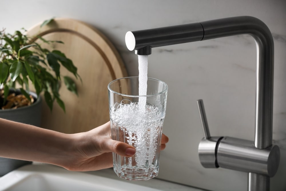 person filling glass with filtered water from sink
